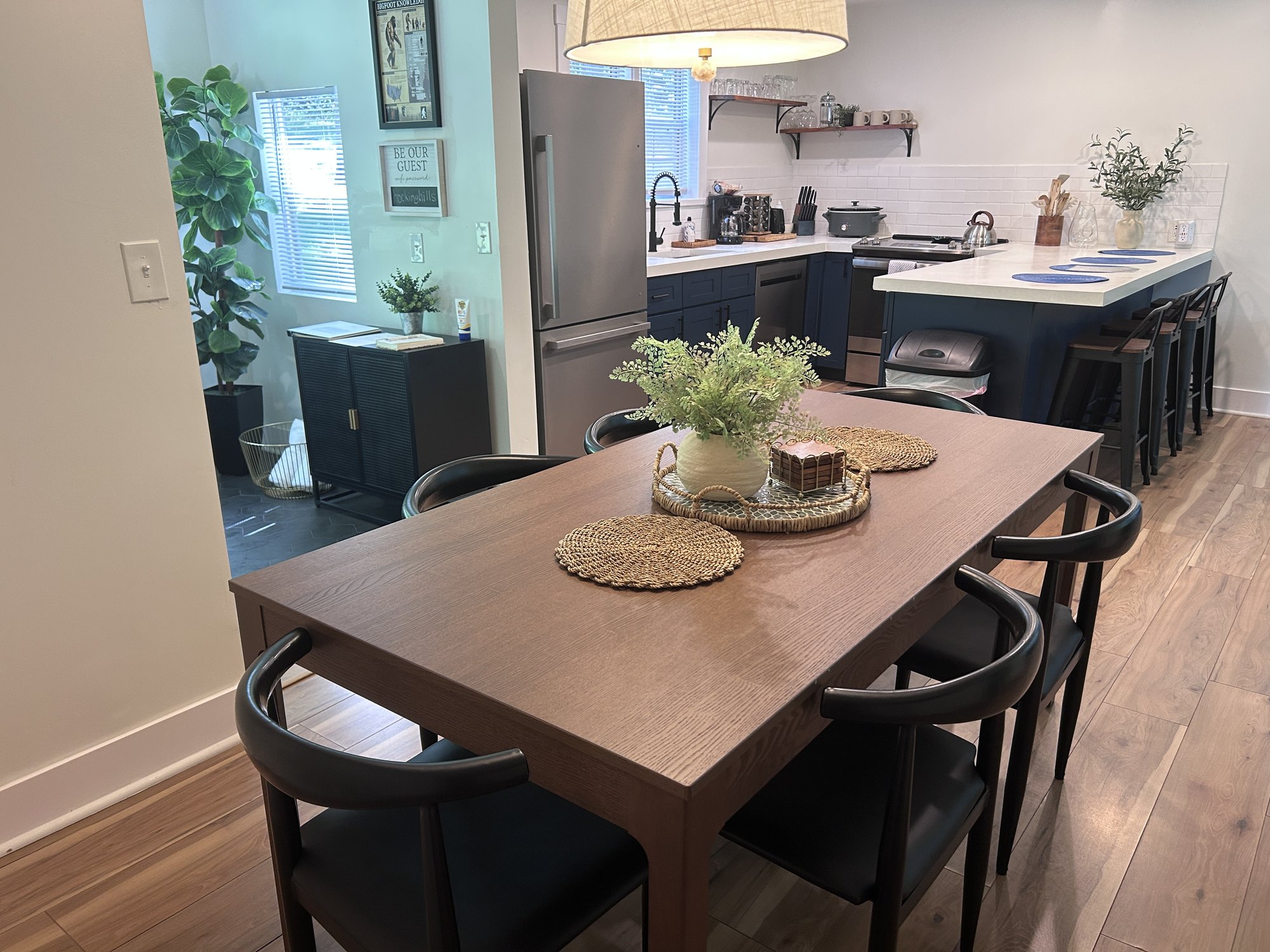 Dining table styled with greenery under a pendant light, kitchen beyond