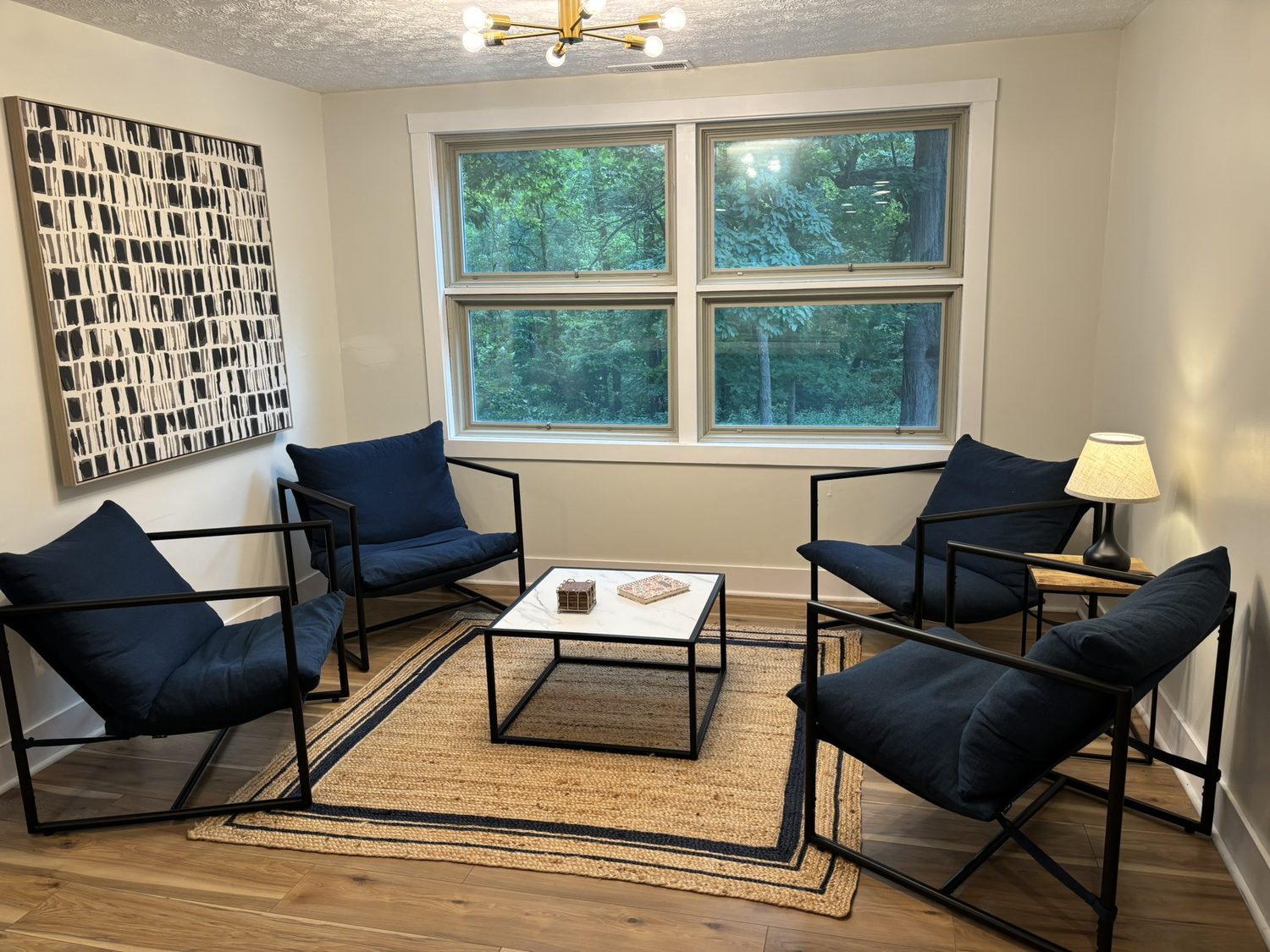 Sitting room with navy lounge chairs beneath a wall of windows looking into the woods