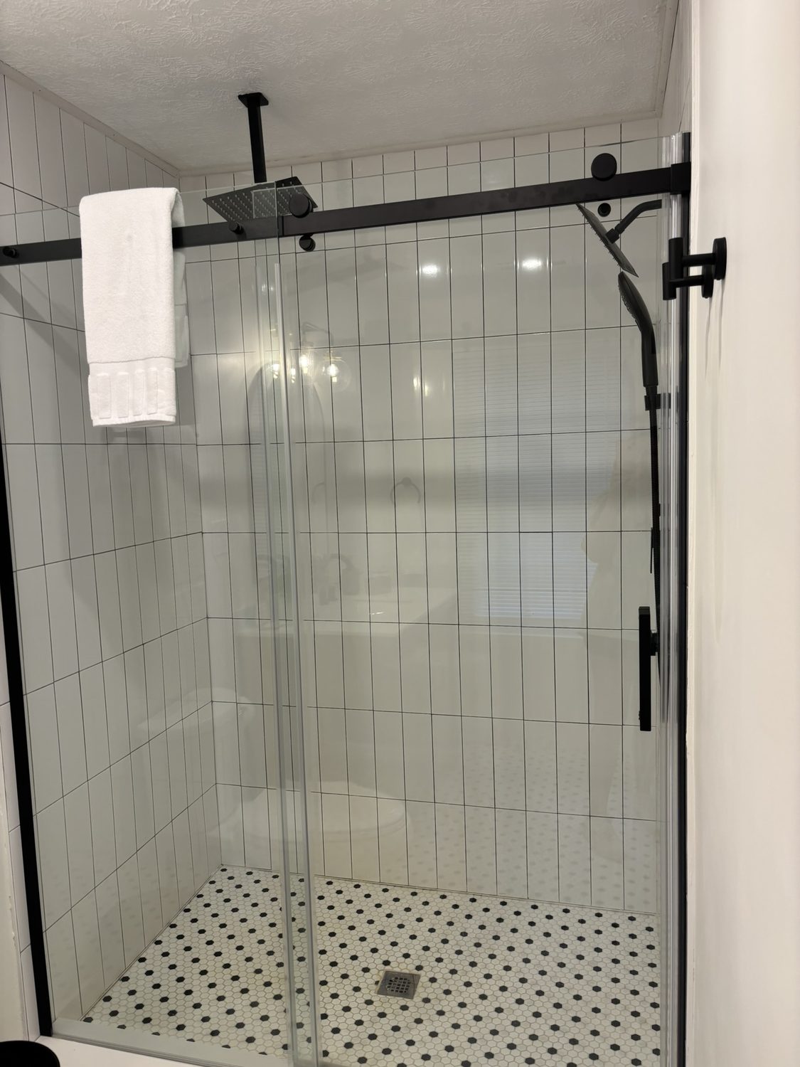 Walk-in glass shower with white tile, matte black fixtures and penny-tile floor