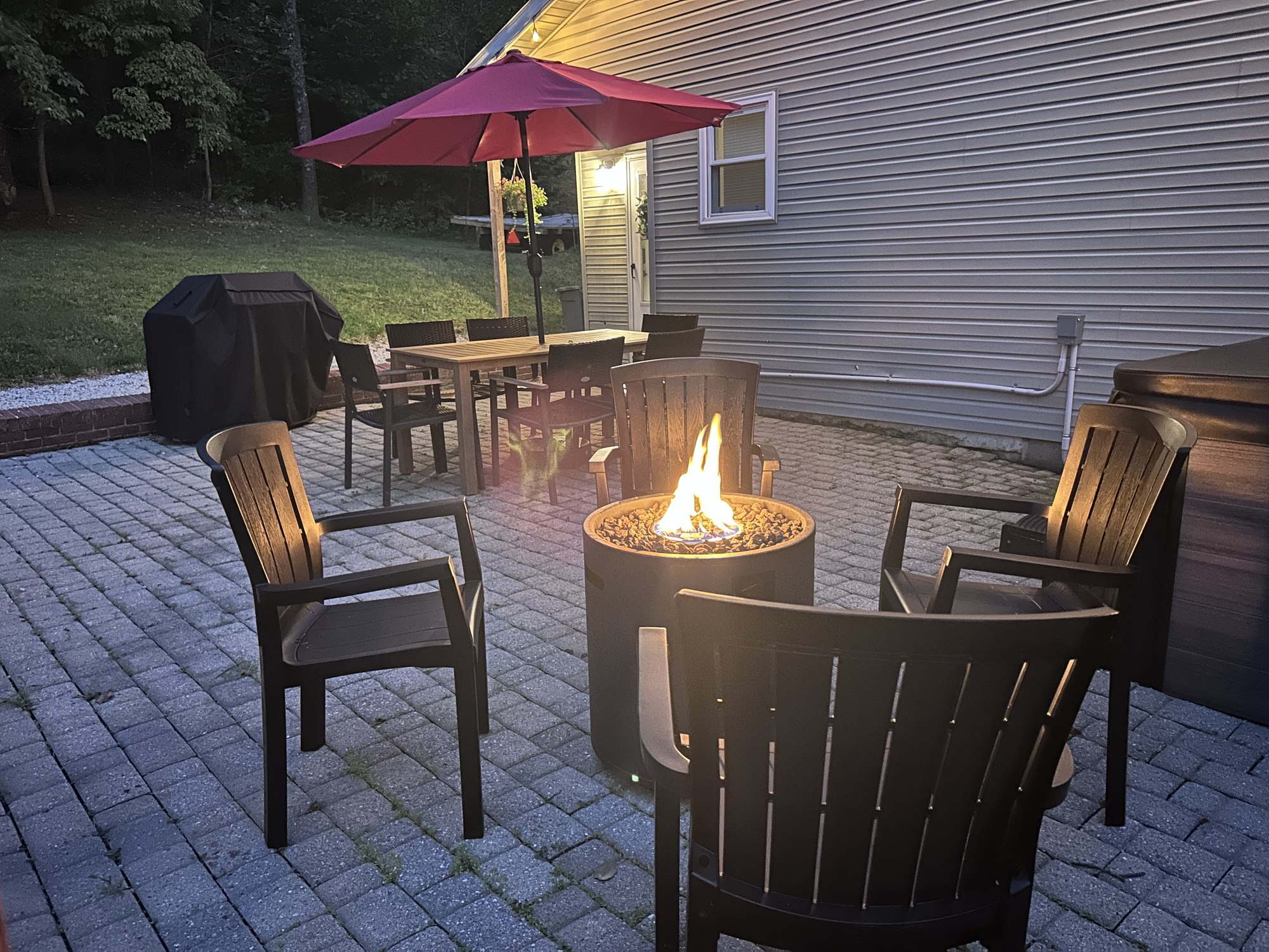 The lit fire pit and the patio table together at dusk, umbrella up
