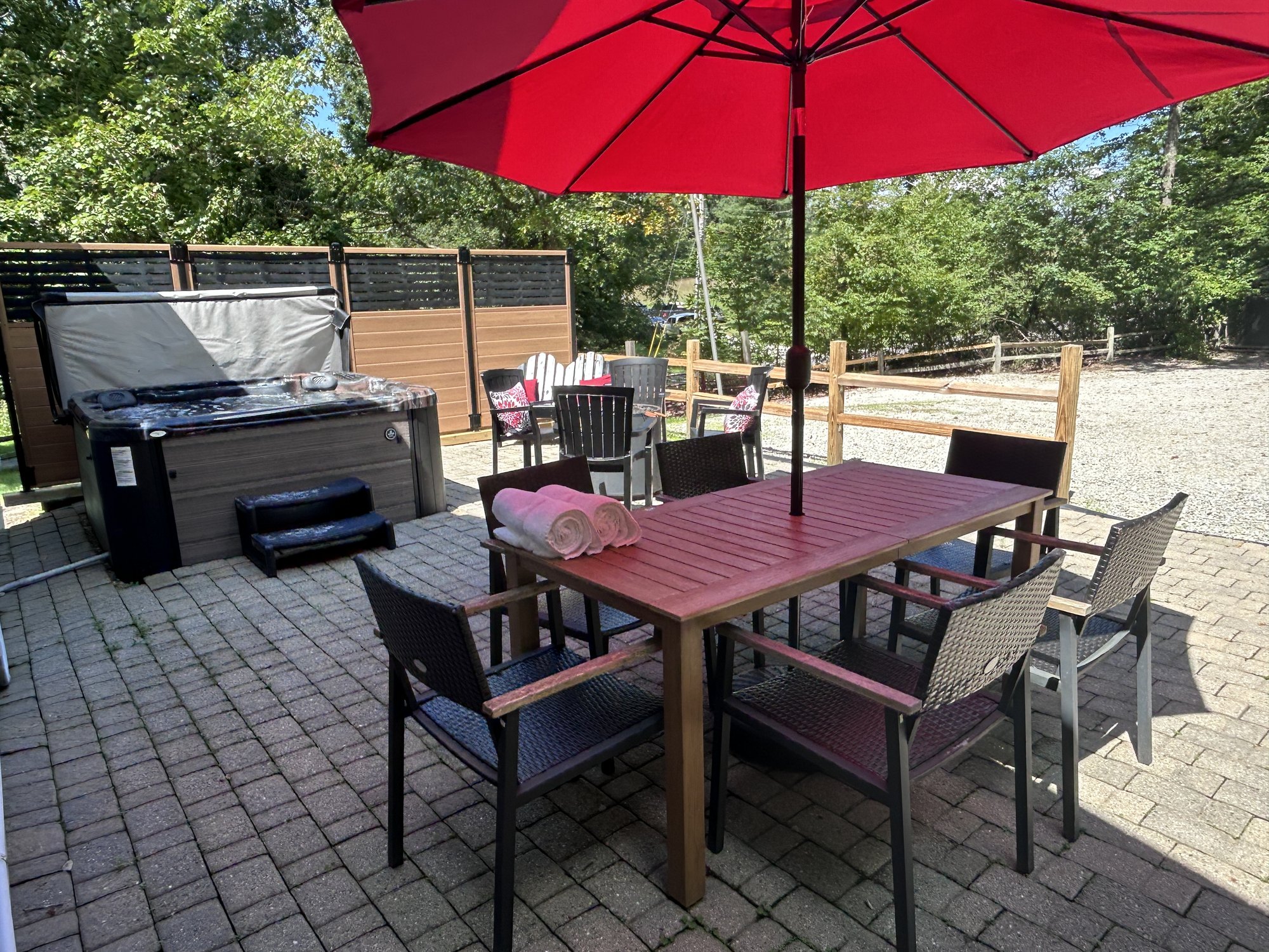 Paver patio with the umbrella up and the table set, hot tub and privacy screen beyond