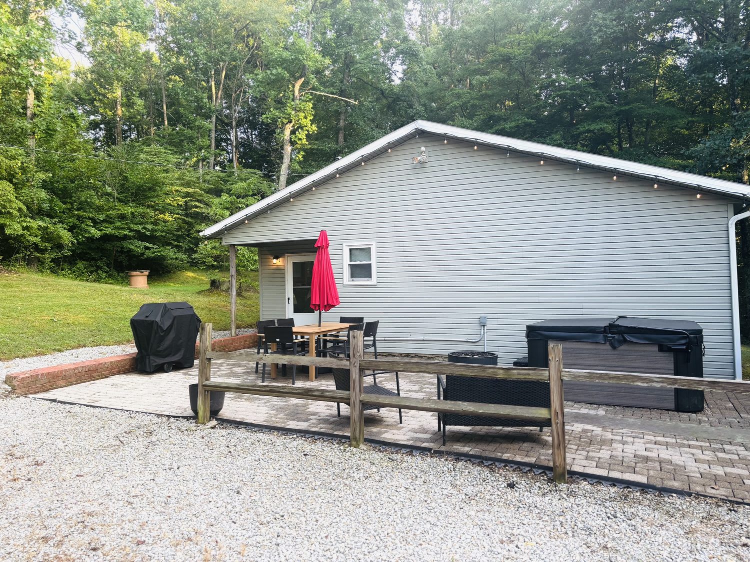 Covered patio, hot tub and grill against the wooded backdrop