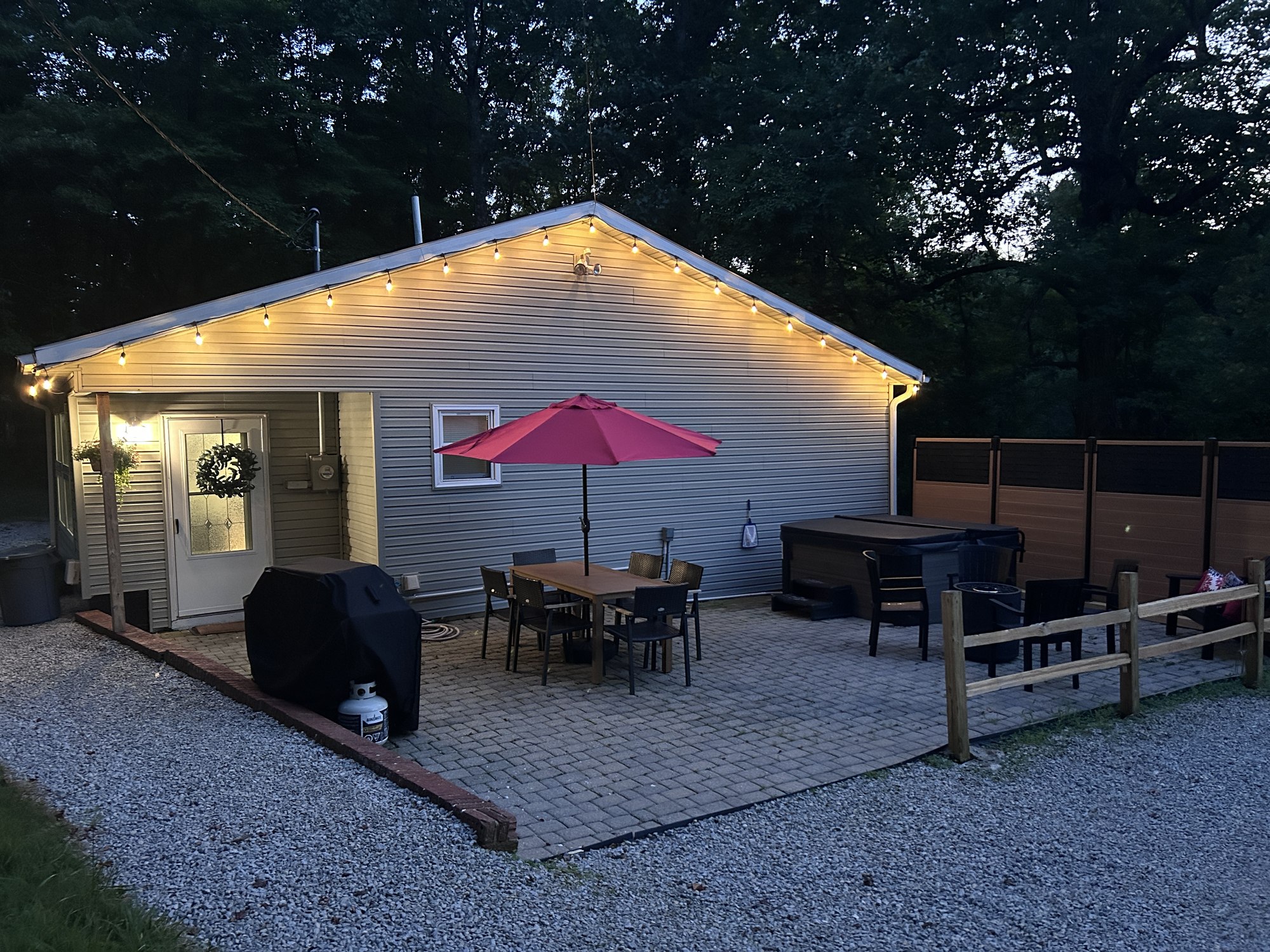The patio at dusk with the string lights lit along the gable and the porch light on