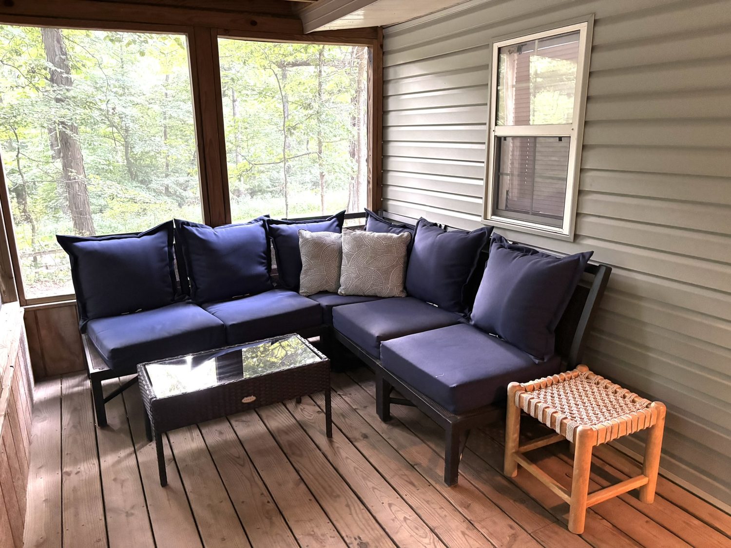 Screened porch with a navy sectional looking out into the trees